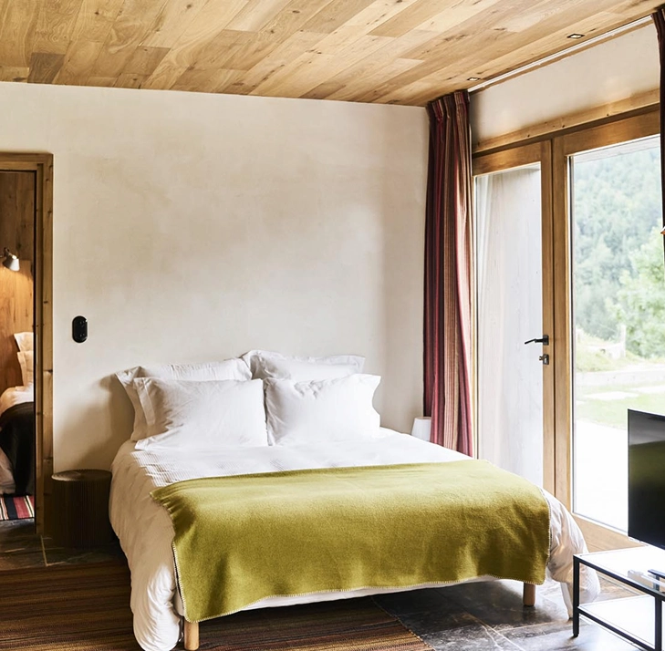 Chambre cosy avec lit et plaid vert, ouverture sur l'extérieur
