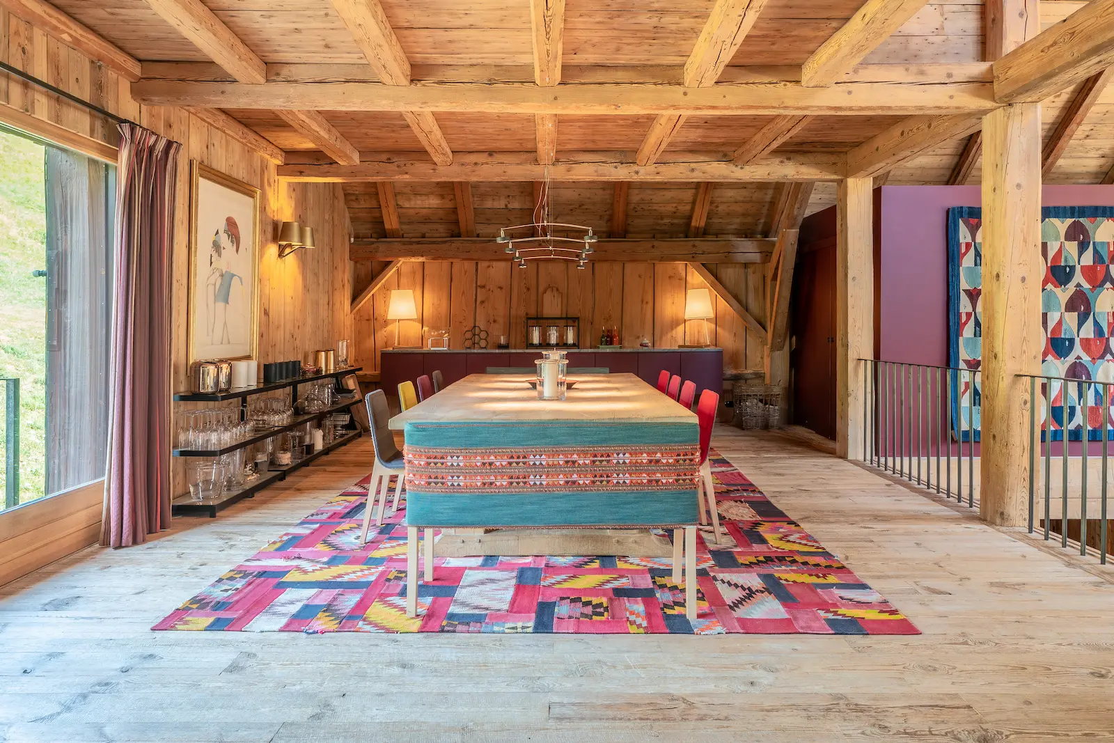 Salle à manger sous charpente bois avec table dressée et tapisseries murales