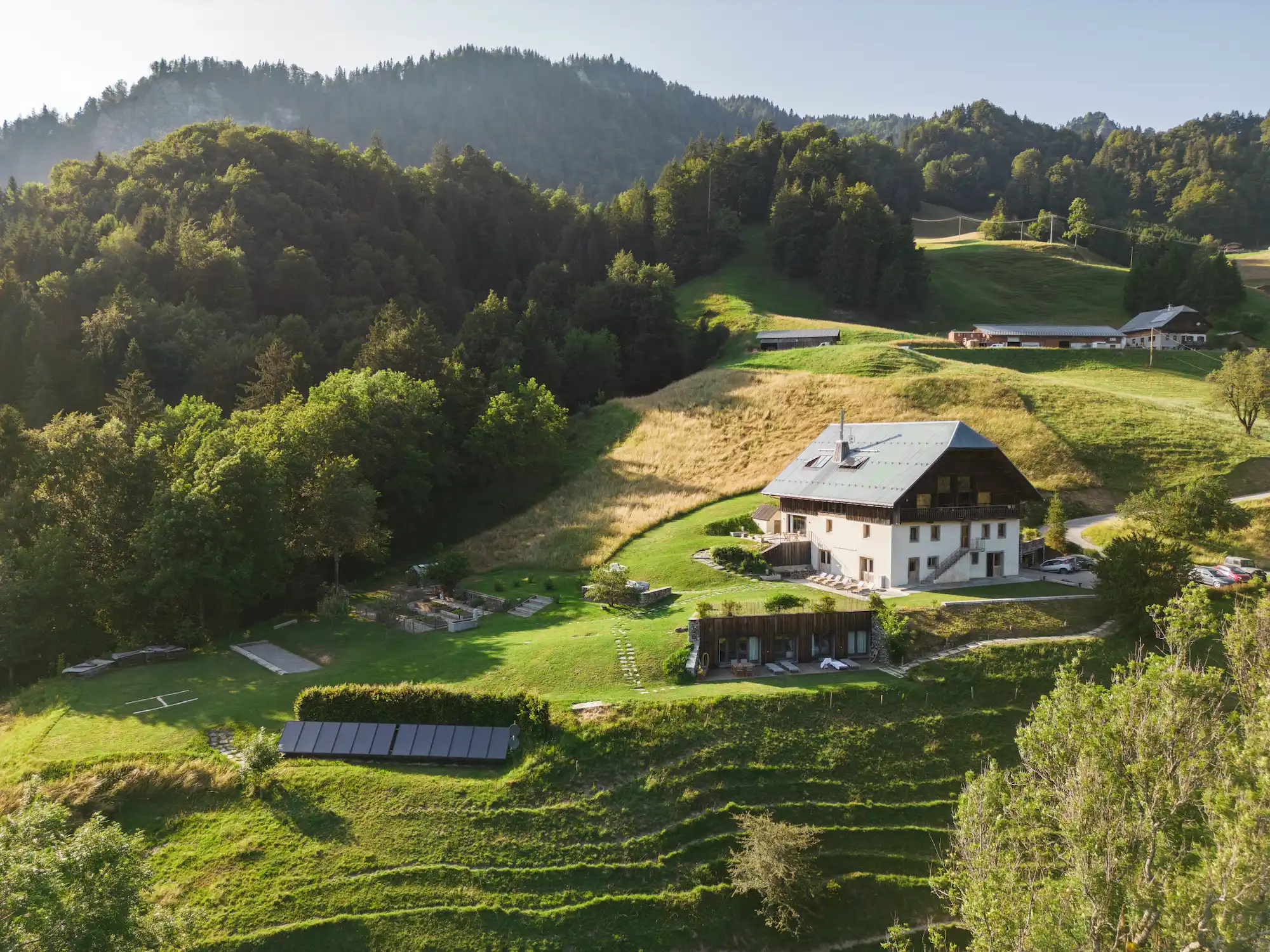A drone aerial view of the Ferme du Passieu and its grounds, surrounded by meadows and forests in the summer.