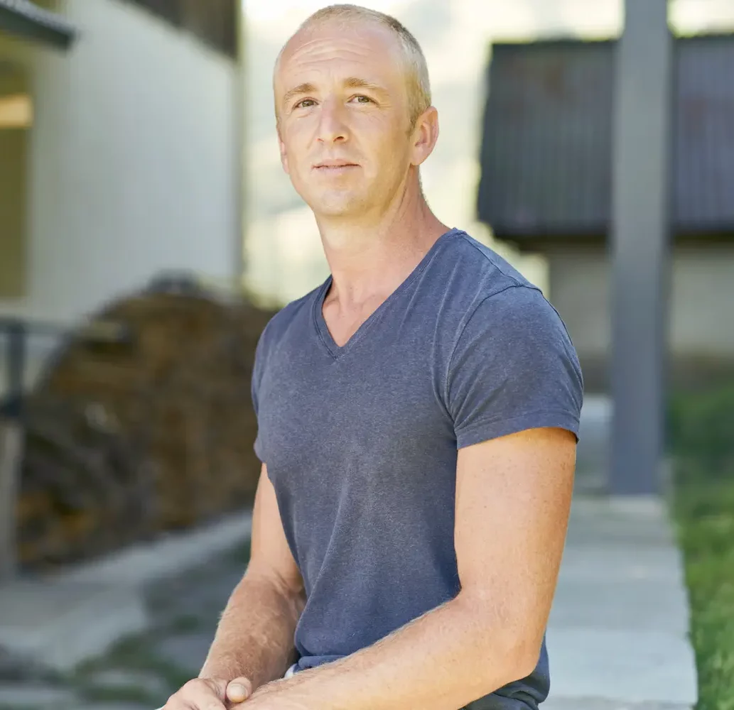 Portrait de Lionel en extérieur devant un bâtiment en bois