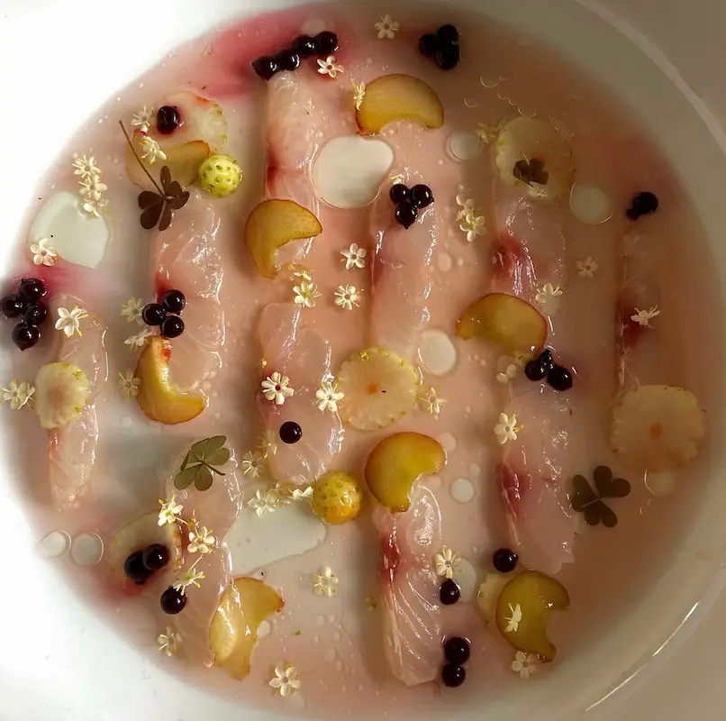 Assiette gastronomique de poisson cru avec fruits rouges et fleurs comestibles
