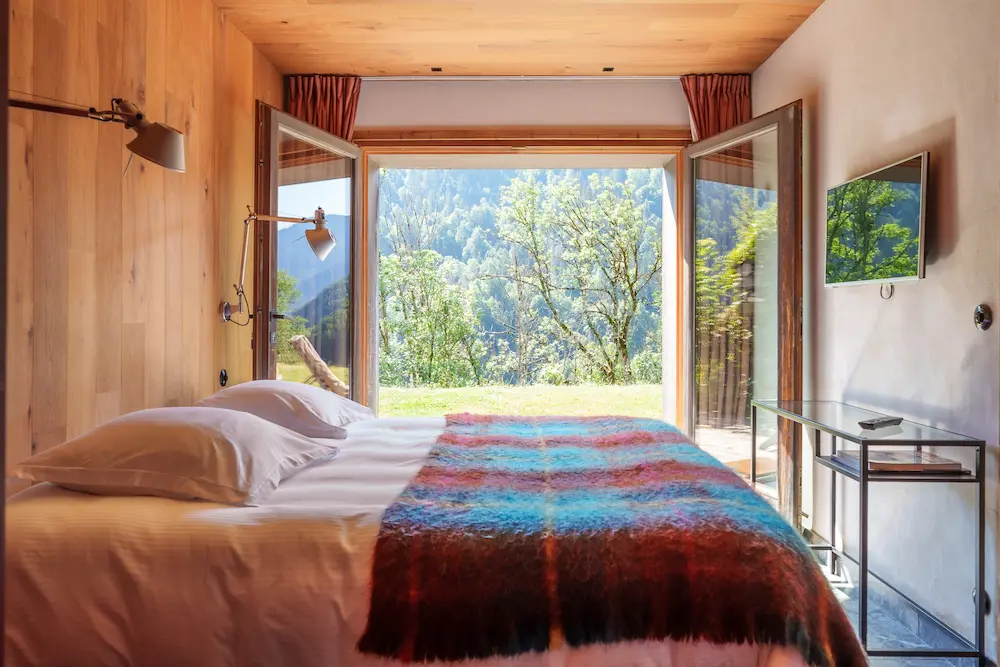 L'Annexe – chambre avec baie vitrée ouvrant sur la prairie et plaid coloré