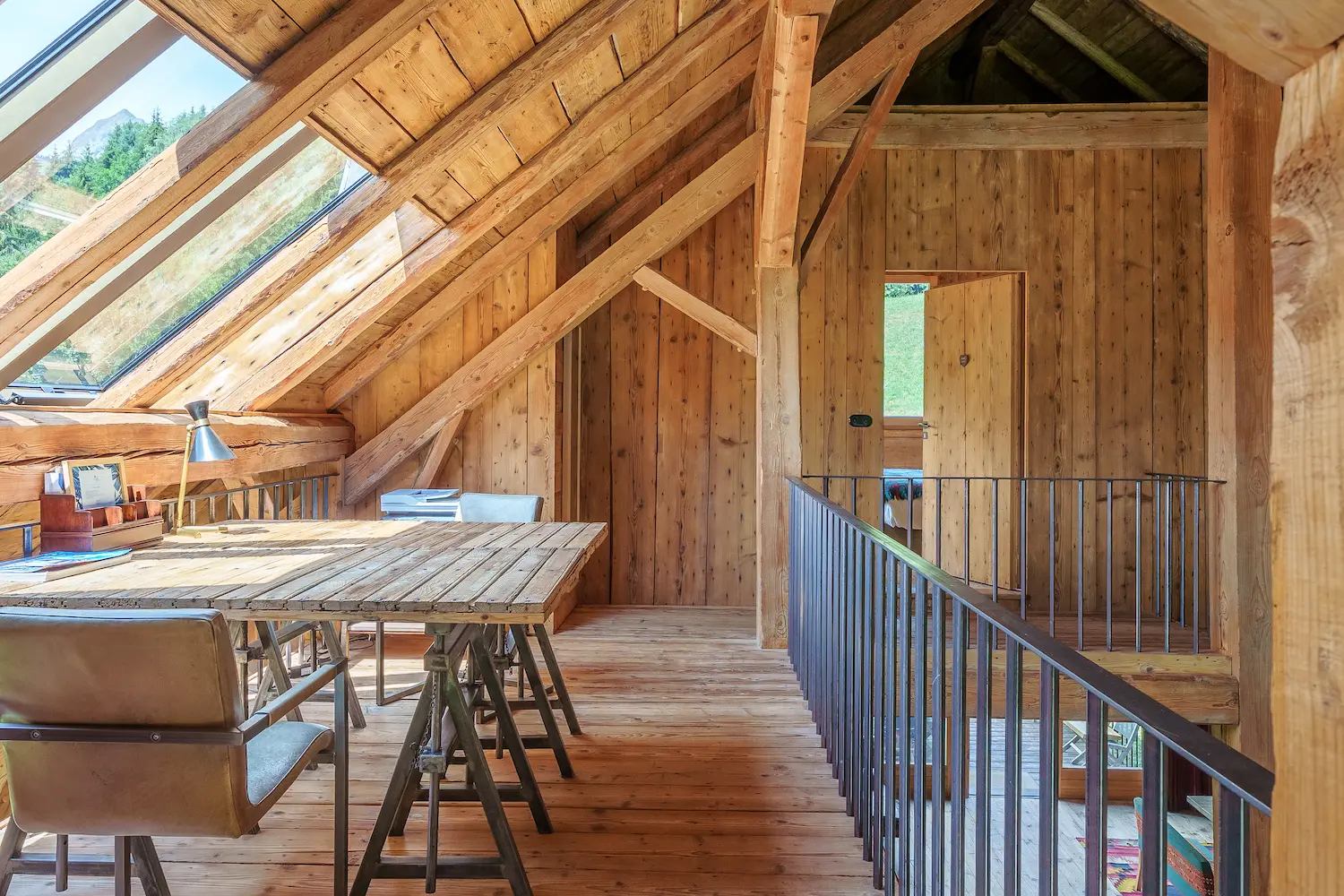 Mezzanine aménagée en bureau avec grande table en bois sous charpente et velux