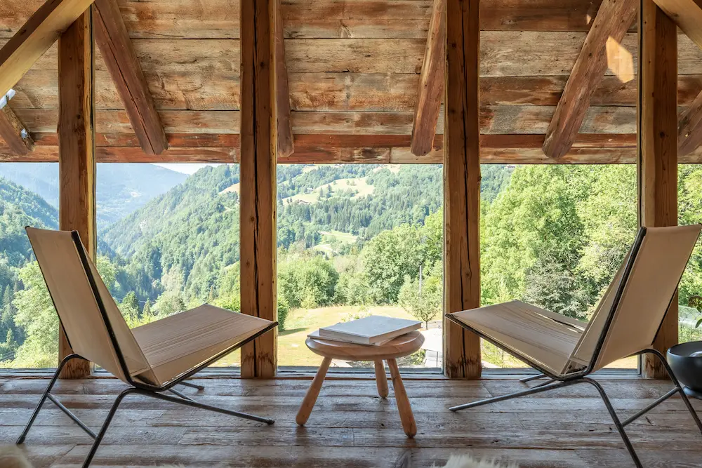 Chaises longues blanches et repose-pieds sur une terrasse en bois face à la forêt