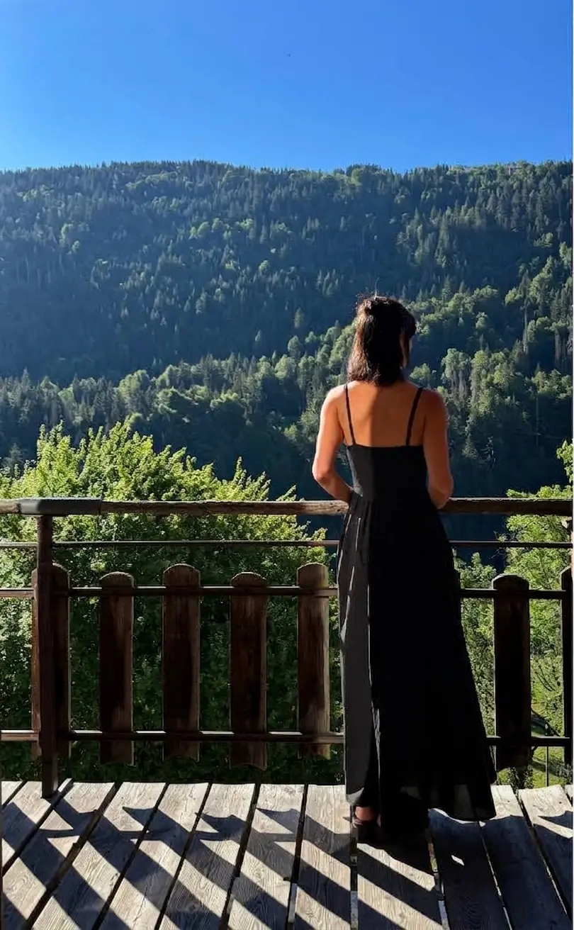 Femme en robe noire de dos, profitant de la vue sur la vallée boisée depuis la terrasse