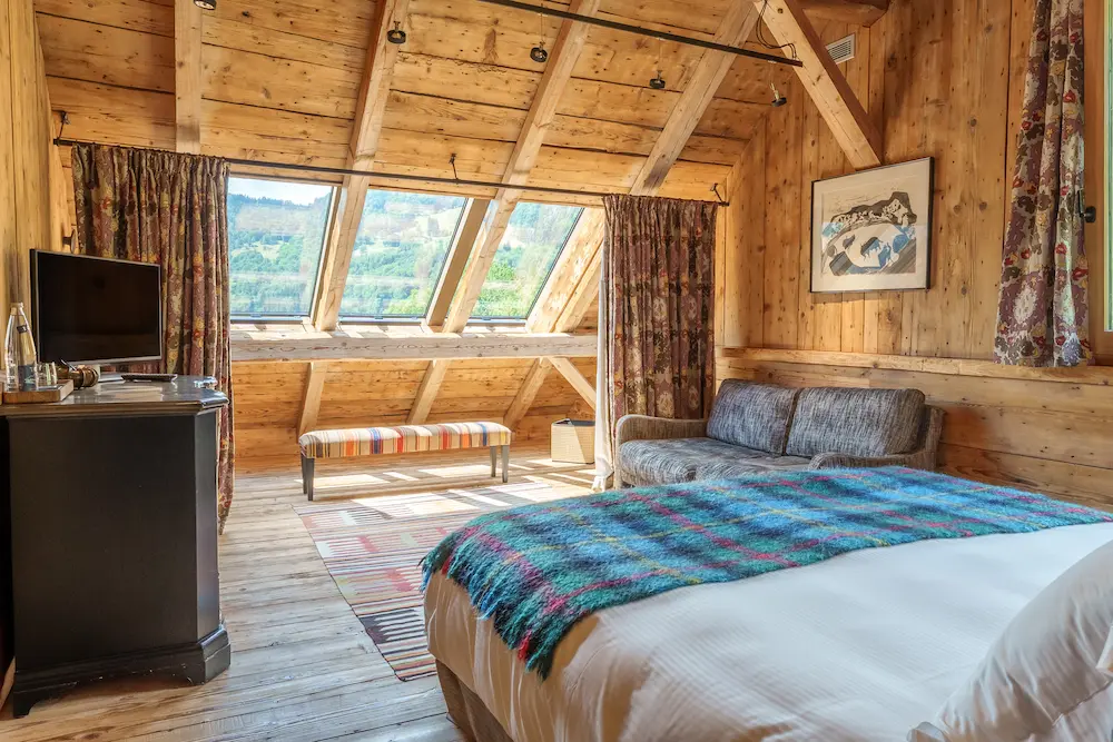 Suite Master – chambre mansardée avec lit double, banquette et vue sur la vallée