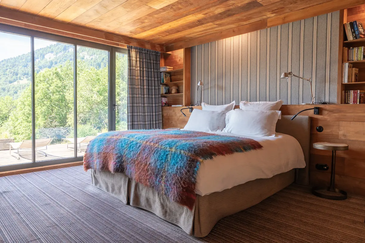 Chambre Teck – lit double devant une grande baie vitrée avec vue sur la vallée et la forêt